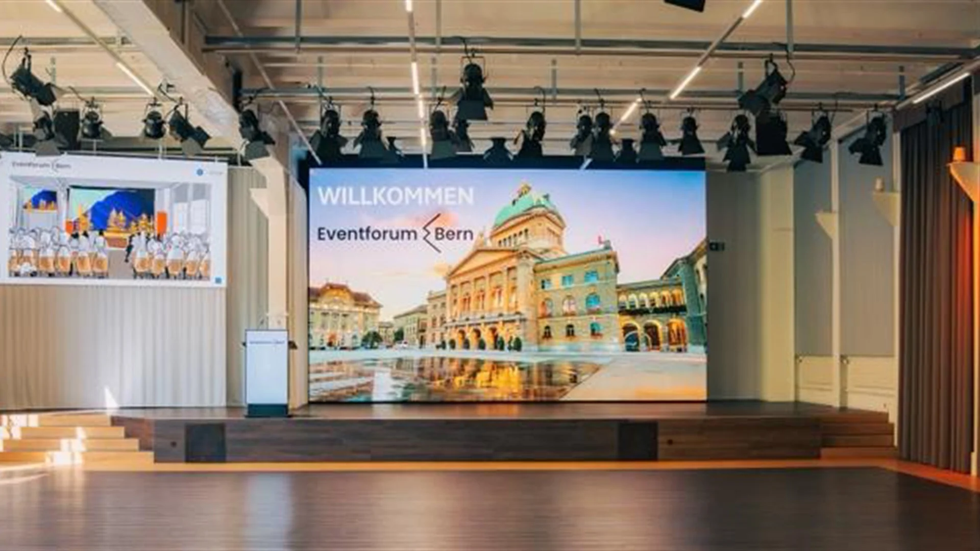 Bühne mit zwei LED-Wänden und Willkommensgruss auf dem Bundeshaus-Motiv im Eventforum Bern.