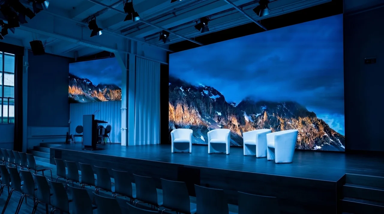 Bühne mit LED-Wänden, weissen Sesseln und bestuhltem Zuschauerbereich für eine Veranstaltung im Eventforum Bern.