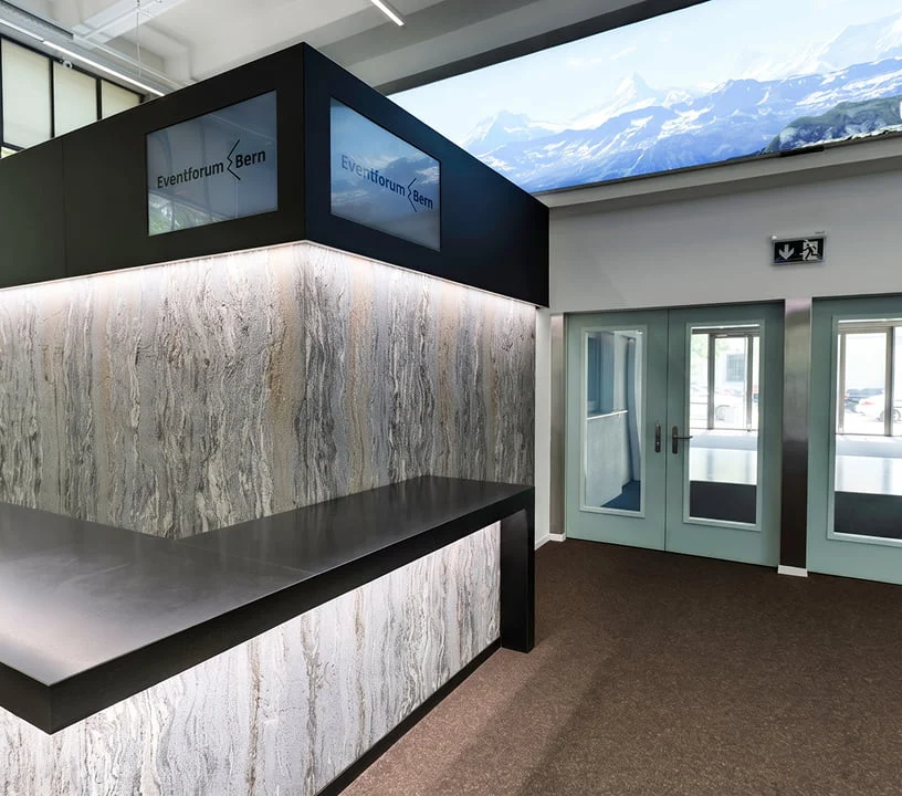 Empfangstheke mit beleuchteter Steinoptik und Eingangstüren im Eventforum Bern.