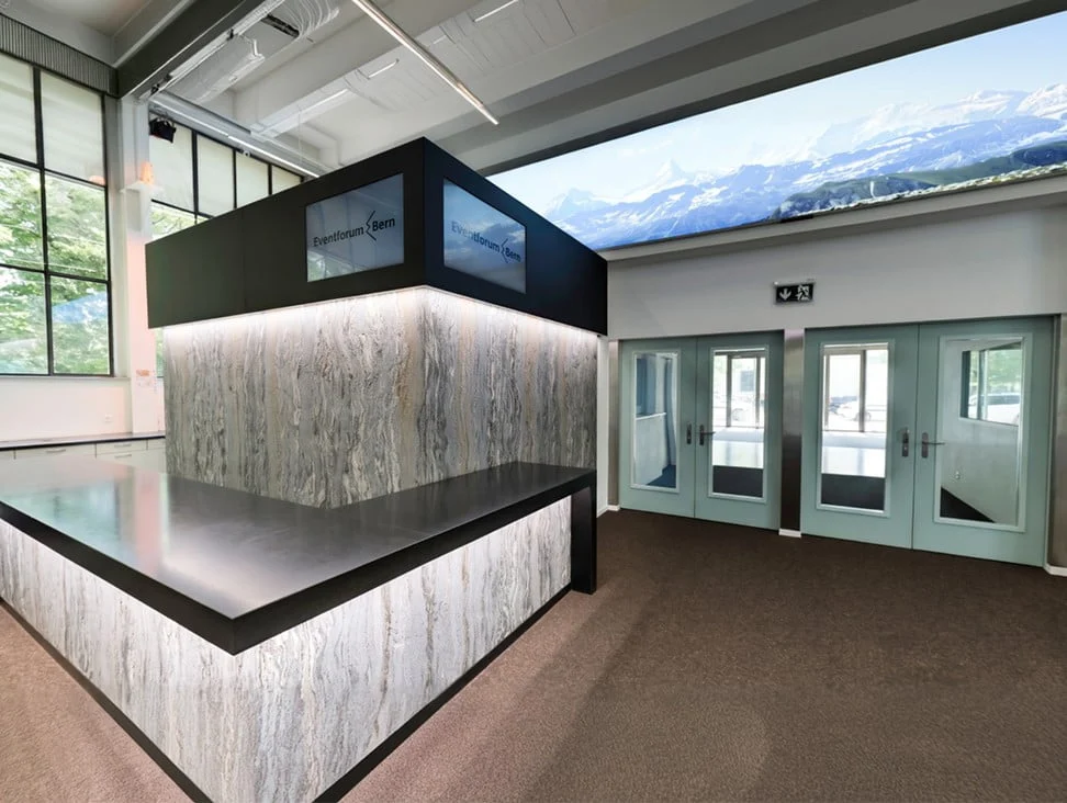 Empfangstheke mit beleuchteter Steinoptik und Eingangstüren im Eventforum Bern.