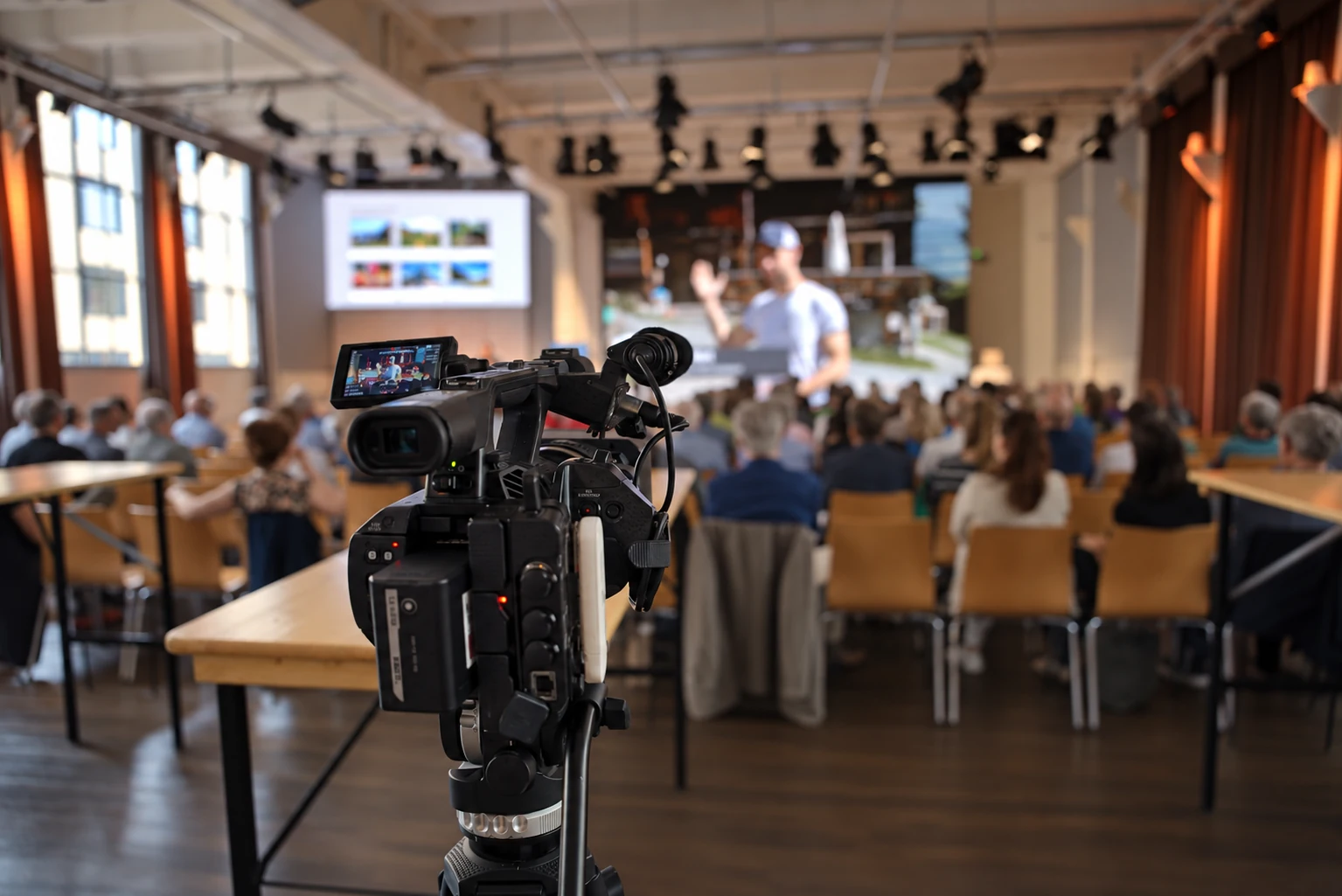 Professional video camera in front of an audience and presentation displays at Eventforum Bern.