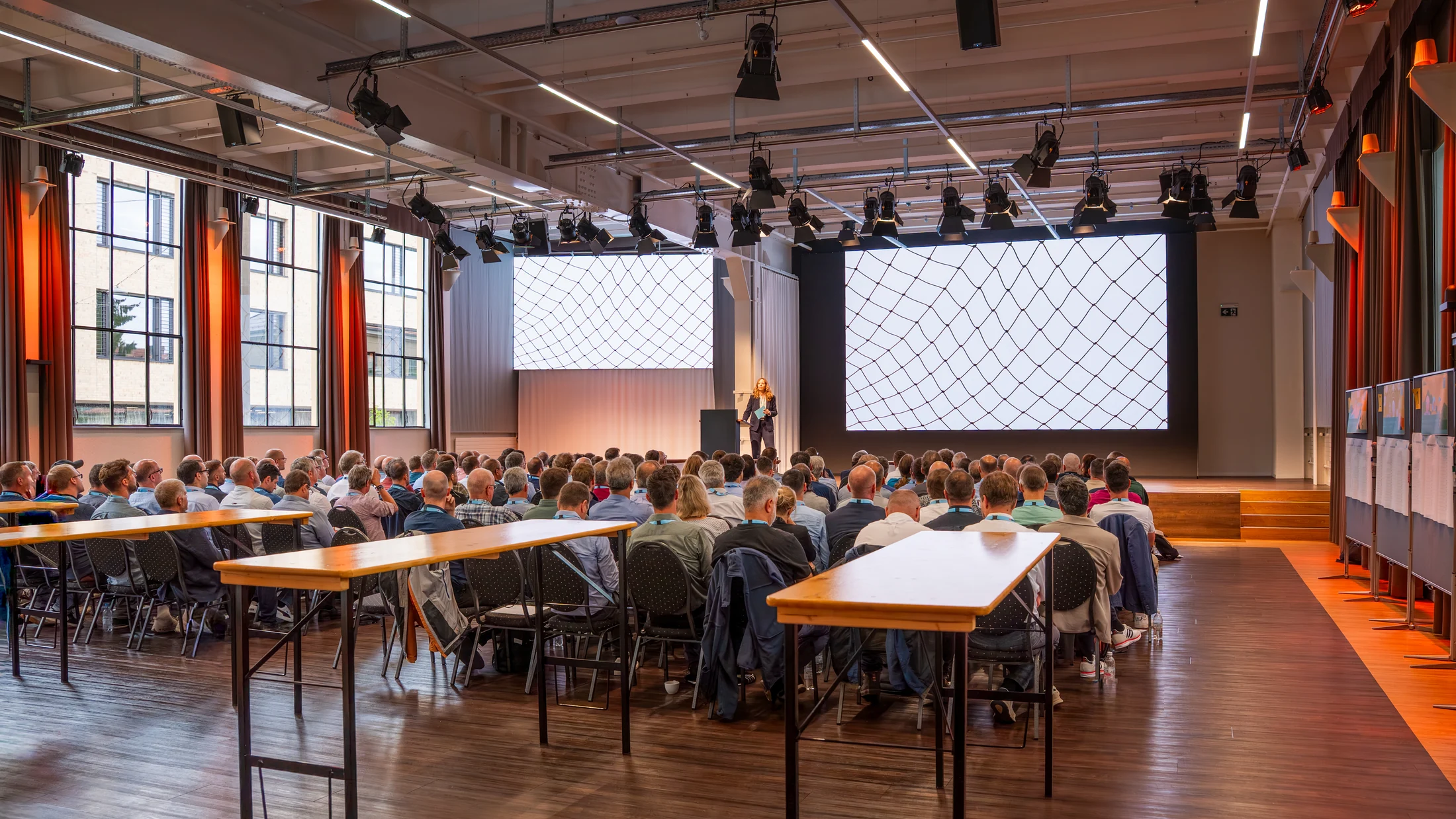 Training participants at seminar tables in the bright plenary hall.