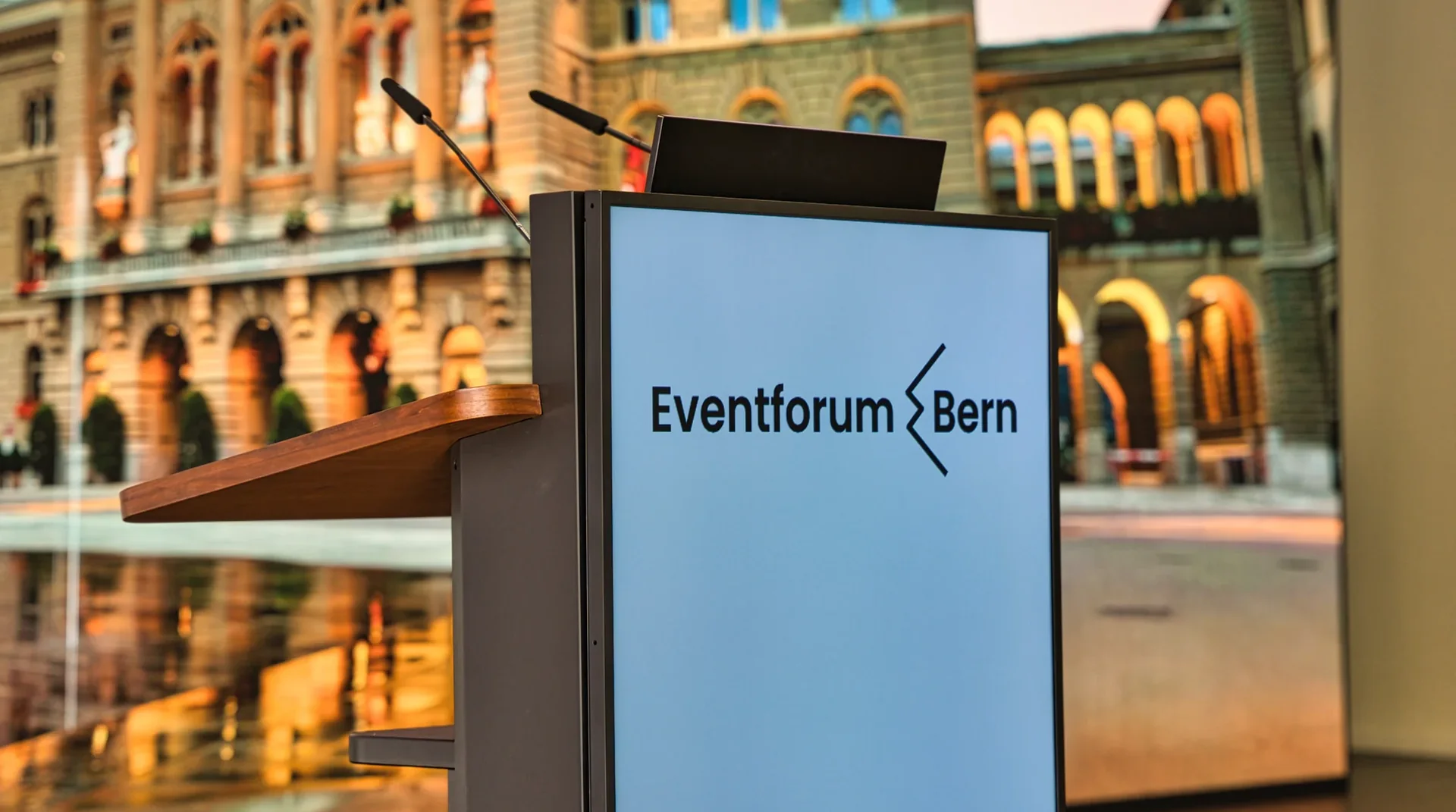 Rednerpult mit Eventforum-Bern-Logo und Mikrofonen vor der LED-Wand mit dem Bundeshaus