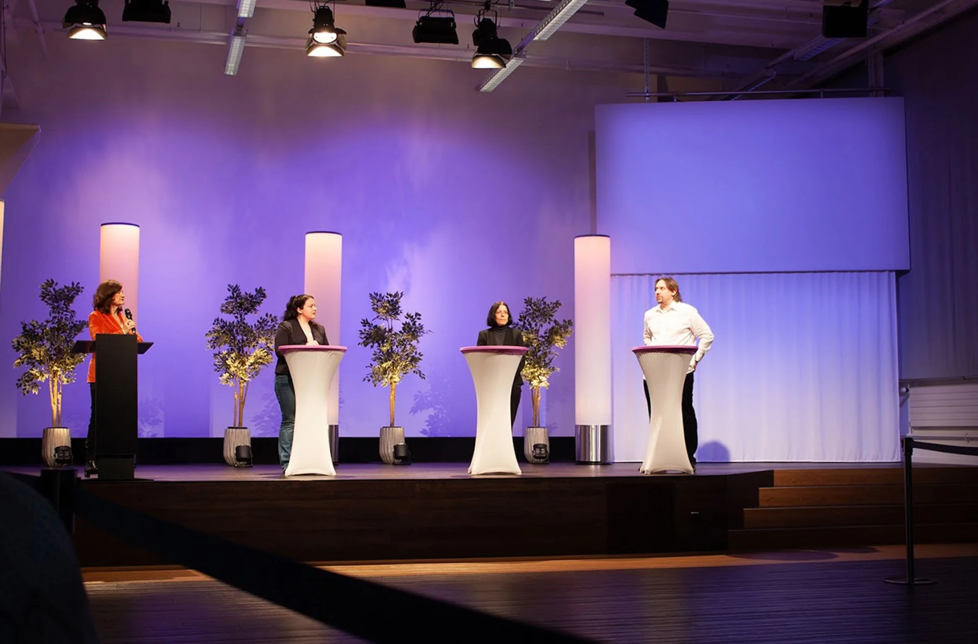 Podiumsdiskussion auf einer beleuchteten Bühne mit Stehtischen und Mikrofon im Eventforum Bern.