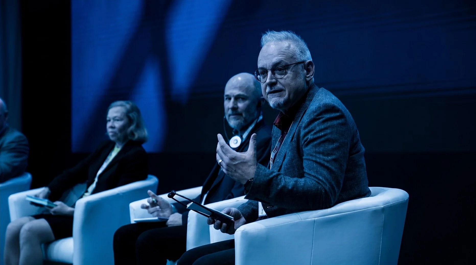 Podiumsteilnehmender spricht mit Mikrofon während einer blau beleuchteten Veranstaltung im Eventforum Bern.