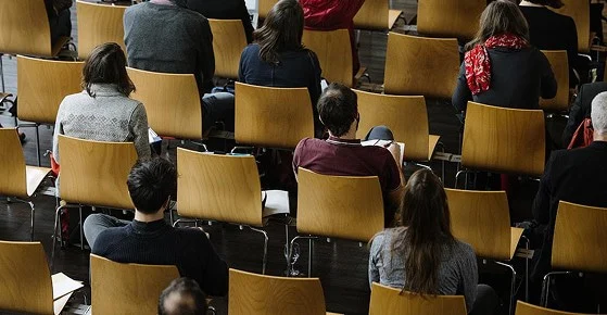 Publikum sitzt auf Holzstühlen während einer Veranstaltung im Eventforum Bern.