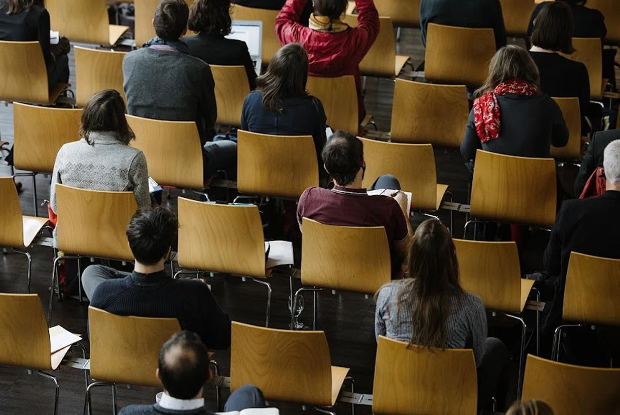 Publikum sitzt auf Holzstühlen während eines Vortrags im Eventforum Bern.