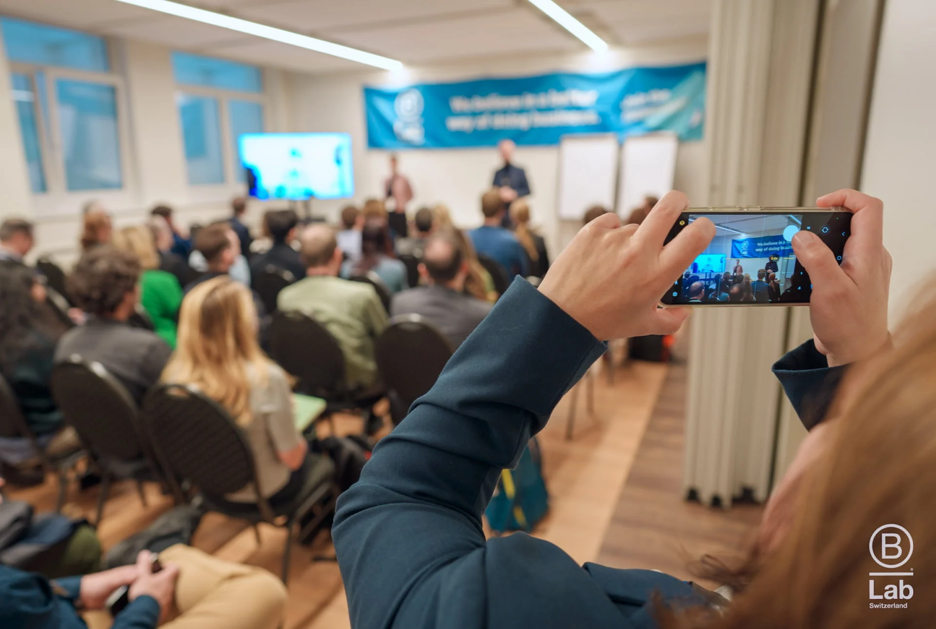Person nimmt einen Vortrag vor Publikum mit dem Smartphone auf im Eventforum Bern.