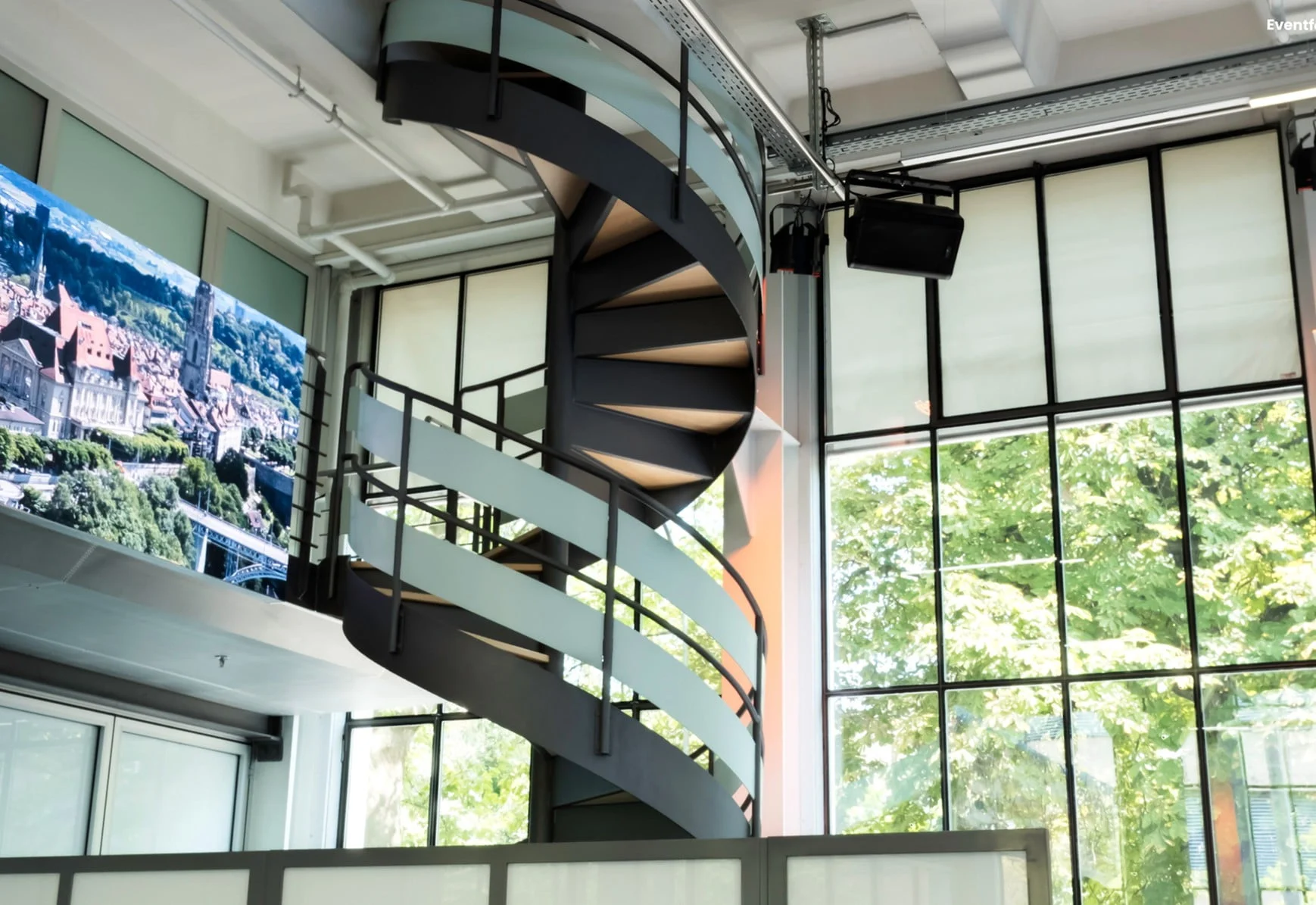 Wendeltreppe mit grosser Fensterfront und Monitor in der Eventhalle des Eventforum Bern.
