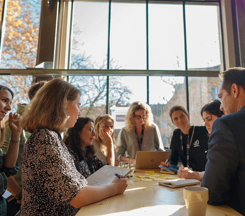 Teilnehmende arbeiten gemeinsam in einer Workshop-Runde am Tisch.