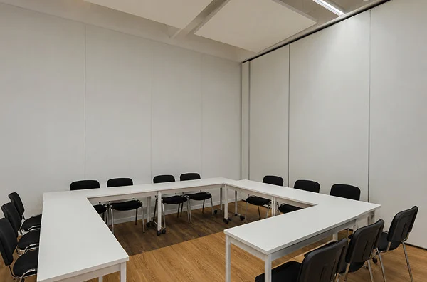 Workshopraum mit U-förmig angeordneten Tischen und Stühlen.